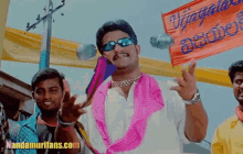 a man wearing sunglasses and a pink scarf is standing in front of a banner that says ' vijayalaya ' on it
