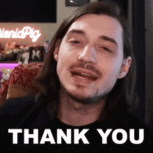 a man with long hair and a beard is sitting in front of a thank you sign