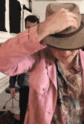 a man wearing a pink jacket and a hat adjusts his hat