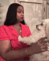 a woman in a pink shirt holds a small dog