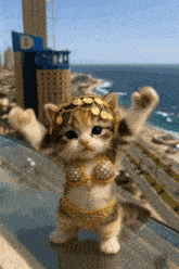 a cat wearing a gold bra and a headdress stands on a balcony overlooking the ocean