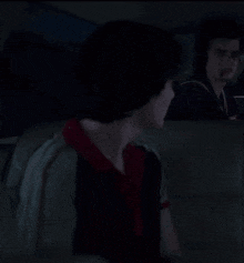 a young man in a black and red shirt is sitting in a dark room .