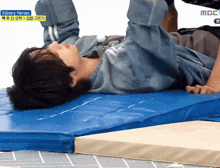 a person laying on a blue mat with xdinary heroes on the bottom right