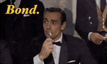 a man in a tuxedo is lighting a cigarette and the word bond is behind him