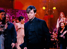 a man in a black suit is standing in front of a crowd