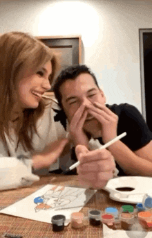 a man and a woman are sitting at a table laughing while painting .
