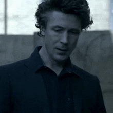 a man with curly hair wearing a suit and a black shirt