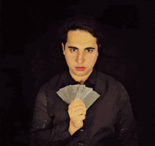 a young man in a black shirt is holding a fan of playing cards