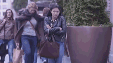 a group of women are walking down a street with a large potted plant in the background .