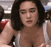 a woman with a very large breast is looking at the camera while wearing a white tank top .