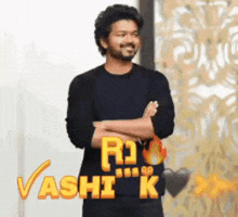 a man in a black shirt is standing with his arms crossed in front of a wall with the word rashi k on it .