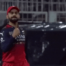 virat kohli is wearing a red and blue jersey and a red hat .