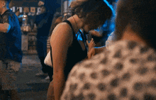 a woman in a black tank top stands in a crowd of people