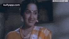 a woman in a yellow and white saree is smiling and looking at the camera in a movie .