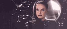a woman in a black dress is standing in front of a mirror with a snake in her hair .