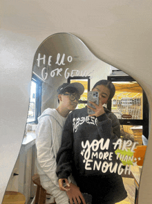 two people taking a picture in front of a mirror that says hello gorgeous and you are more than enough