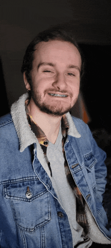 a man wearing braces and a denim jacket smiles for the camera