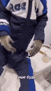 a man in a blue and white jacket is sitting on a toilet with gloves on .