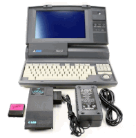 a black and white atari laptop with a charger and a c lab memory card