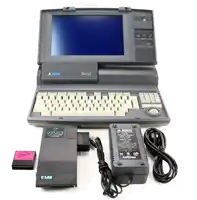 a black and white atari laptop with a charger and a c lab memory card