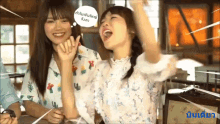 two girls are sitting at a table with their arms in the air and one has a thought bubble that says " ain "