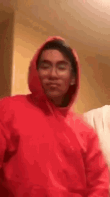 a young man wearing a red hoodie and glasses is taking a selfie .