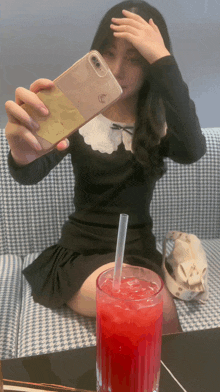 a woman taking a selfie with her phone and a glass of red liquid with a straw