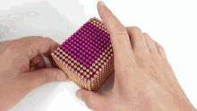 a person holds a cube of pink and gold beads