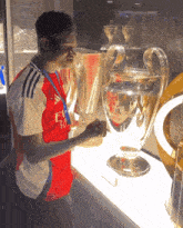 a man in a fly emirates shirt holds a large trophy