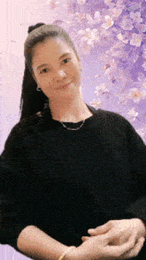 a woman in a black sweater stands in front of a purple flower background