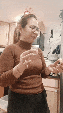 a woman wearing glasses and a birthday hat holds a shot glass in her hand