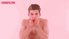 a shirtless man is blowing confetti in front of a pink background with the word cosmopolitan on it