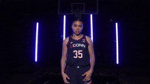 a woman wearing a uconn basketball jersey is pointing at the camera