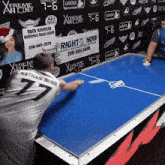 a man in a white shirt with the number 77 on the back is playing air hockey