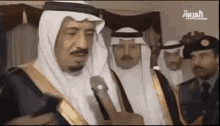 a man in a white robe is talking into a microphone while standing next to a group of men .