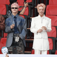 a man with pink hair holds a glass of wine next to another man in a white jacket