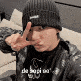 a man wearing a black beanie and a black jacket is making a peace sign with his fingers