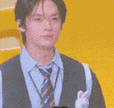 a young man in a suit and tie is clapping his hands in front of a yellow wall .