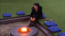 a woman sits in front of a fire pit