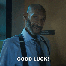 a man with suspenders and a beard is smiling and says good luck