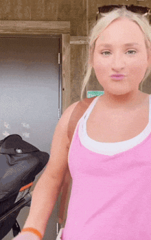 a woman in a pink tank top is standing in front of a door that has a green exit sign on it