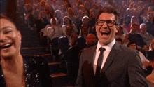 a man in a suit and tie laughs in front of a crowd of people
