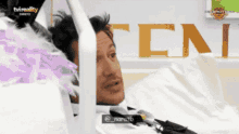 a man laying in a hospital bed with the letters tcn on the wall behind him