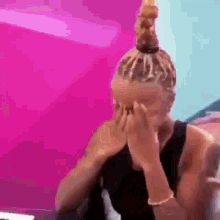 a woman with a bun is covering her face with her hands .