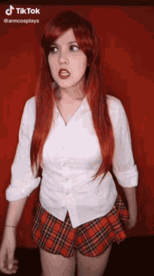 a woman with red hair is wearing a plaid skirt and a white shirt .
