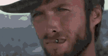 a close up of a man with a beard wearing a cowboy hat and smoking a cigarette .