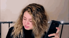 a woman with curly hair is holding a cell phone and making a funny face .