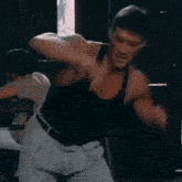 a man in a black tank top is standing in front of a window .