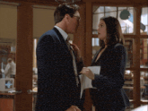 a man in a suit and tie adjusts his tie while a woman in a striped suit looks on
