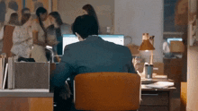 a man in a suit sits at a desk in front of a computer monitor